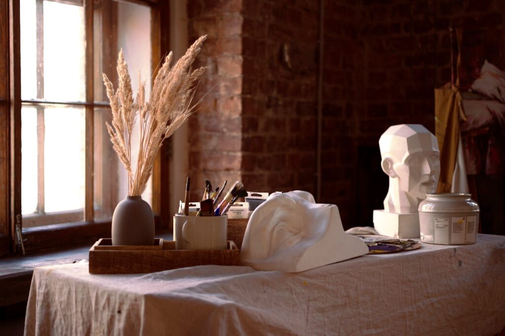 An intimate artist's workspace featuring sculptures, brushes, and dried plants.